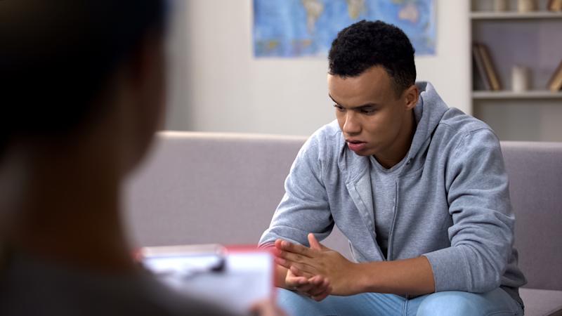 Teenage boy sits in office with adult