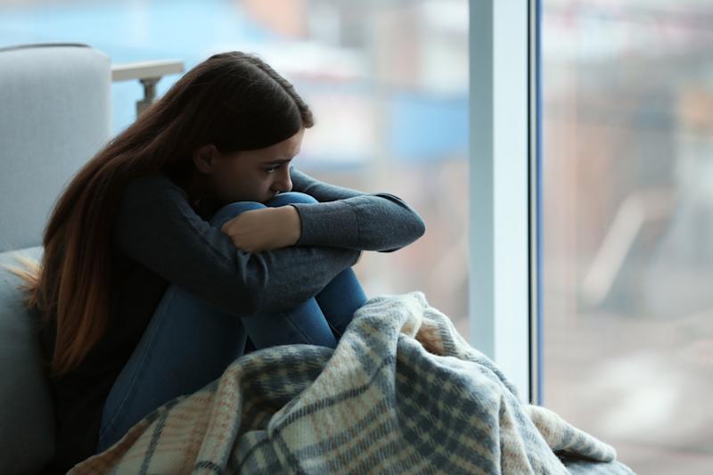 A young woman sits holding her knees with a blanket
